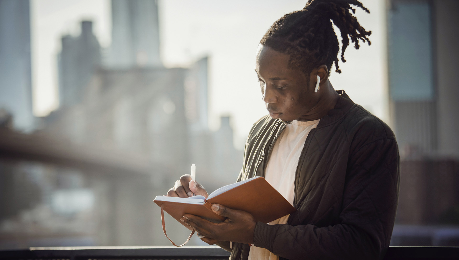 Young man listening to music and writing outdoors